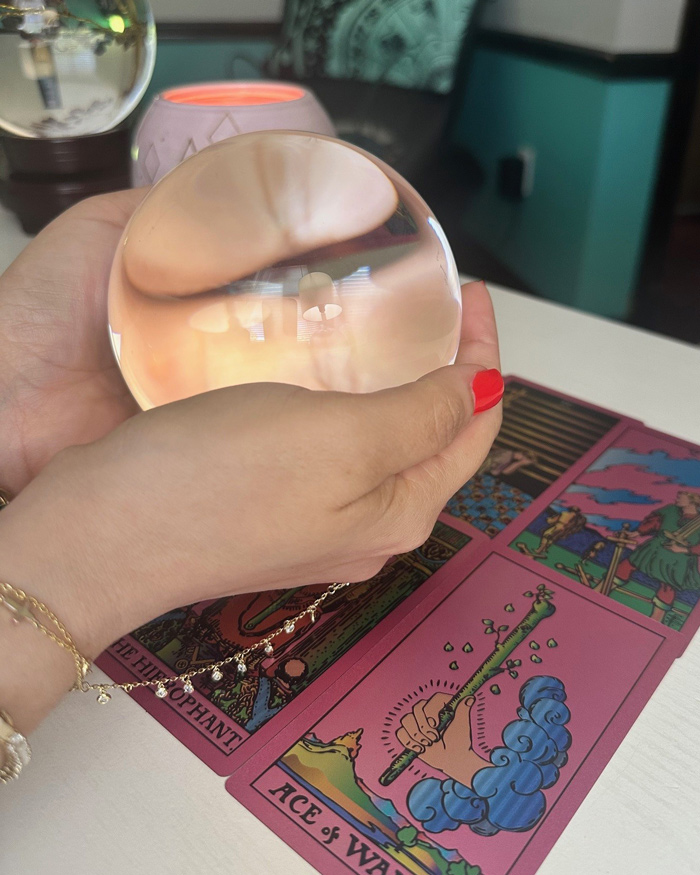 Psychic Dina holds her crystal ball over an array of pink tarot cards.