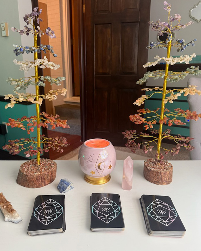 Three piles of tarot cards on a table with candles, crystals, and decorative small trees.