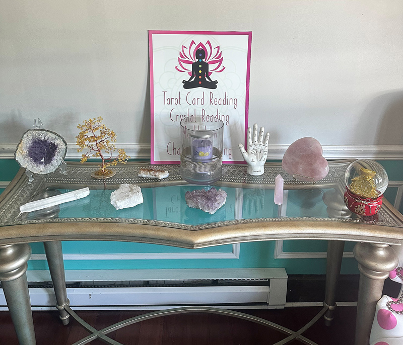 Interior table featuring an amethyst geode, a candle, a rose quartz heart, and a sign listing Tarot Card Reading, Crystal Reading, and more.