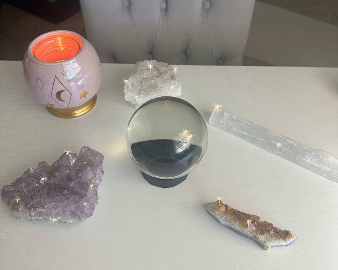 Red rose and crystal ball on a table with rose petals scattered around.