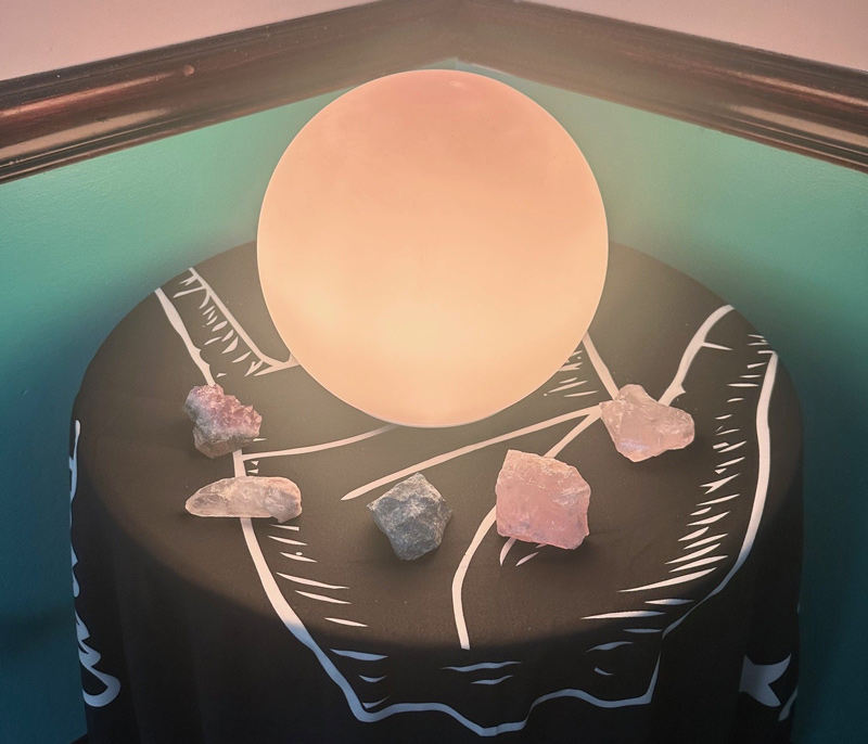 A large glowing ball on a small round table displaying crystals and other stones.