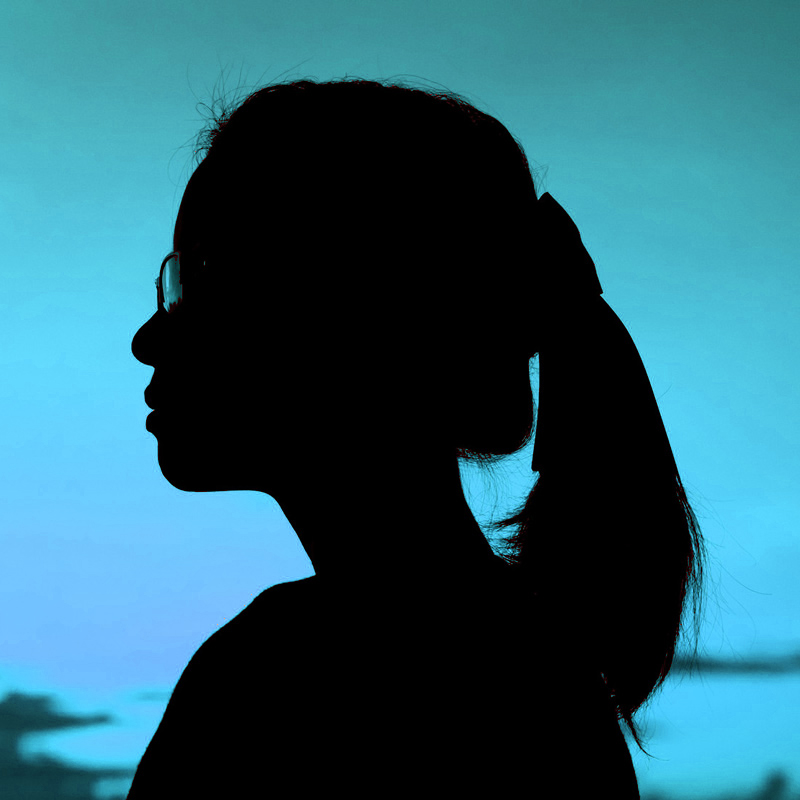 Silhouette of a woman's profile. She is wearing glasses and has a pony tail. The background is a warm red color.